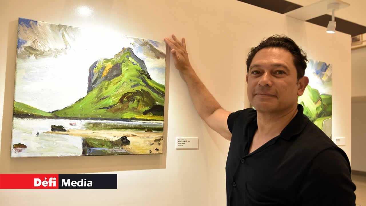 Robert Malherbe posant avec une de ses oeuvres montrant la plage et la montagne du Morne en arrière-plan. MOTHERLAND