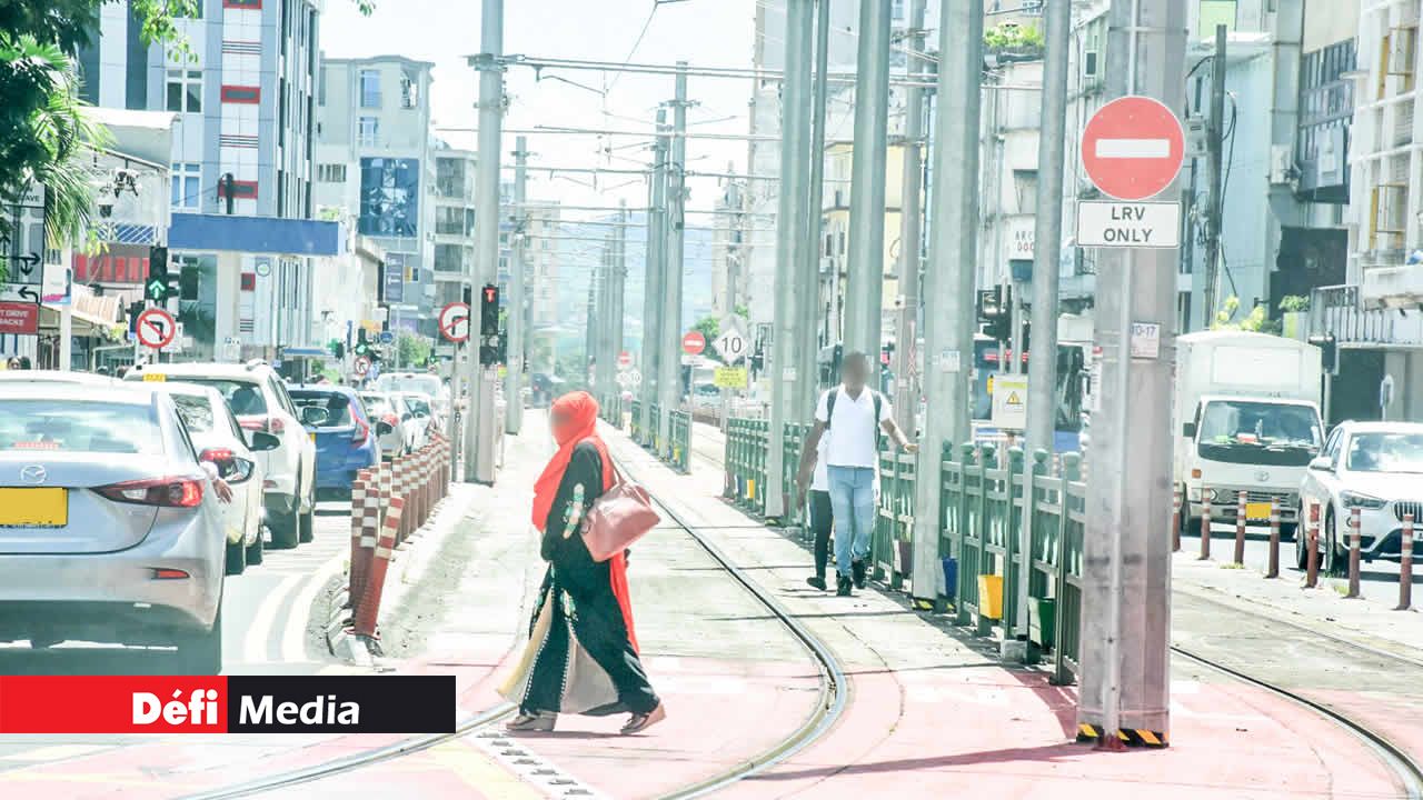Une femme traversant la voie ferrée à Quatre-Bornes, tandis que d’autres piétons marchent le long du corridor du métro, alors qu’il y a un passage clouté.